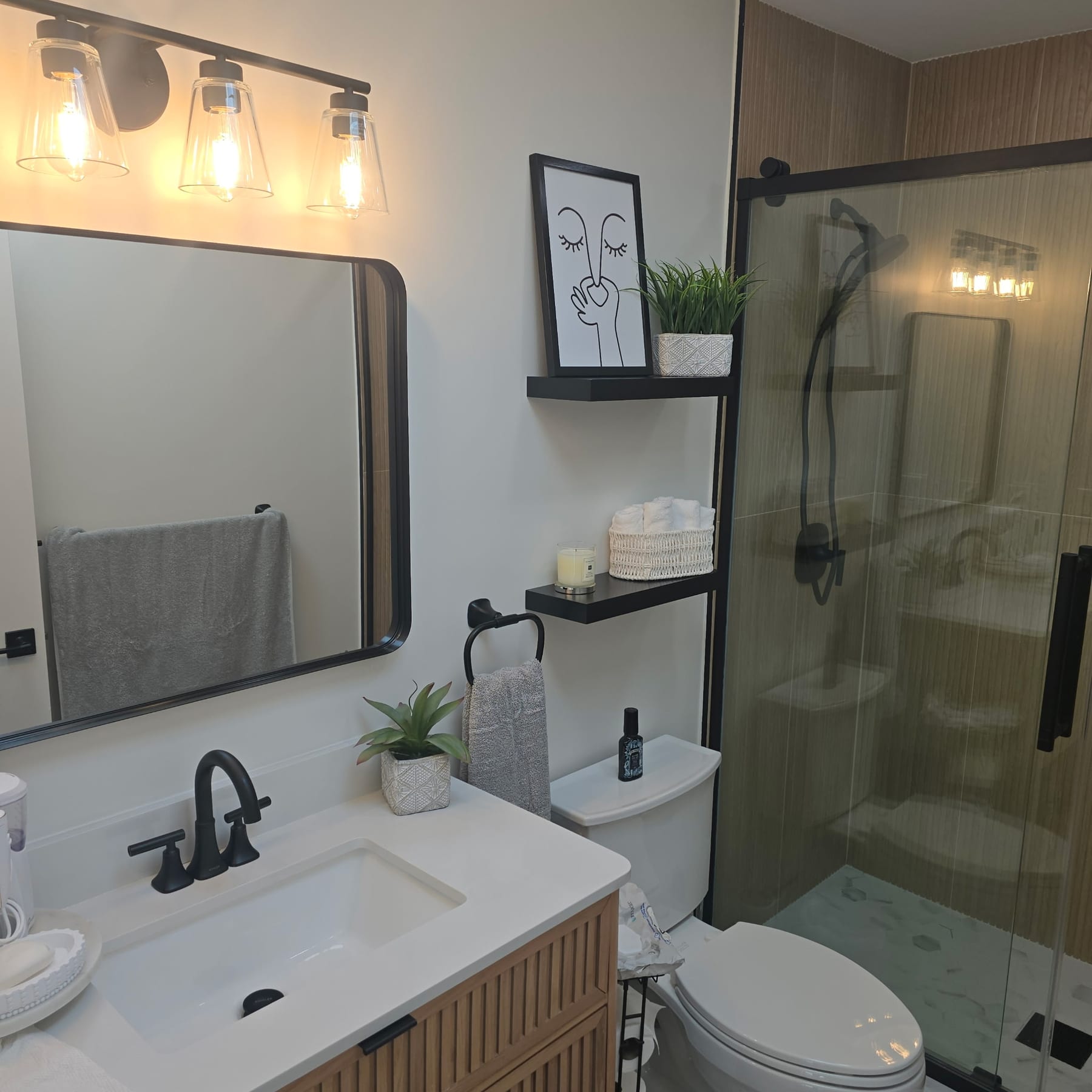 Black-framed vanity with edison-bulb sconces and wood-panel shower